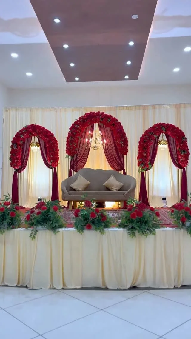 Elegant stage with a sofa, cream drapery and red floral arches for a celebrated couple