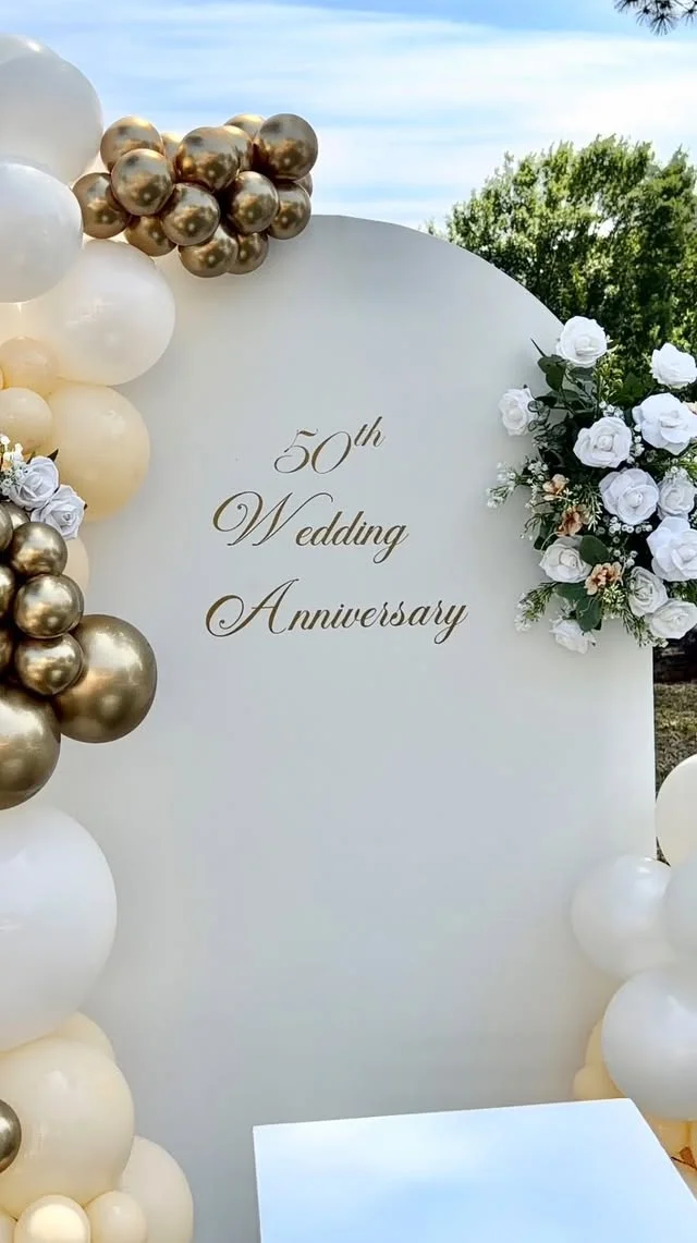 White arch backdrop with soft flowers and gold accents set up as a photo spot