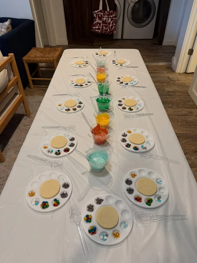 Long table set with cookie decorating palettes, colorful icing cups, and topping bowls