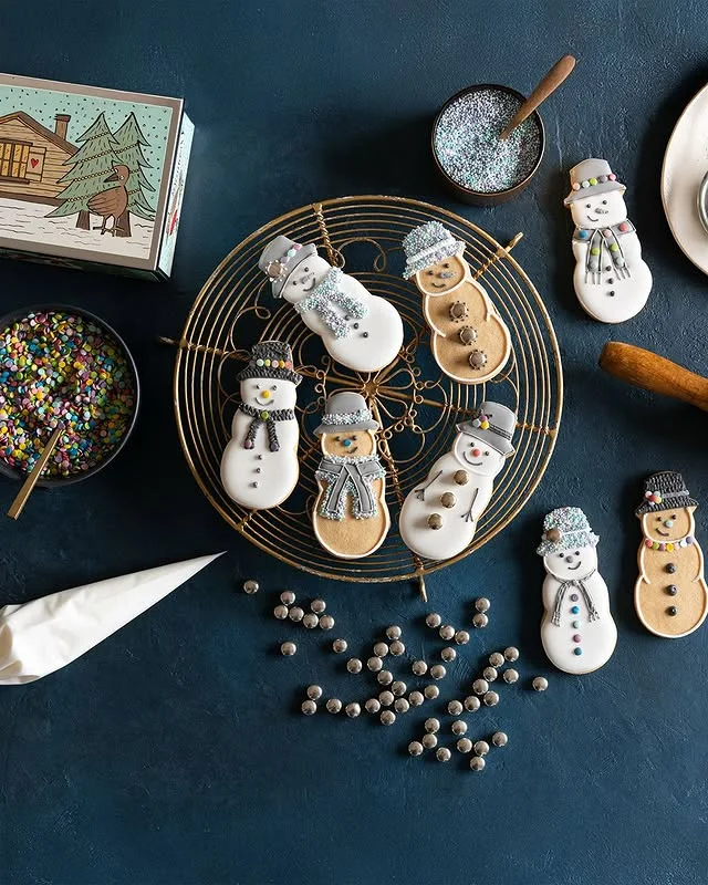 Snowman shaped cookies with scarves and hats arranged on a gold wire cooling rack