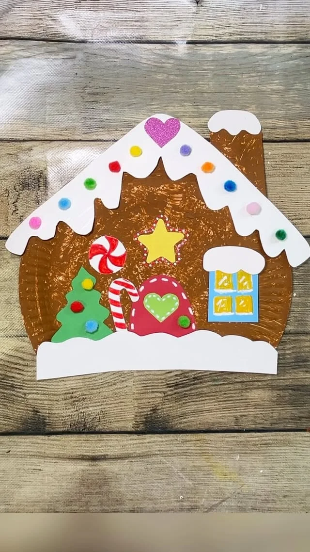 Paper plate gingerbread house craft decorated with pom poms and candy shapes