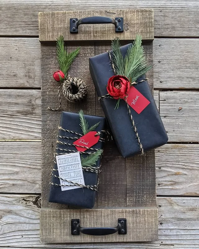 Black wrapped Christmas gift decorated with a red flower, greenery and twine