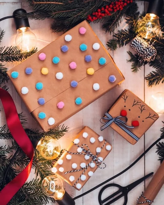 Kraft wrapped gifts covered in colorful pom poms with gingham ribbon