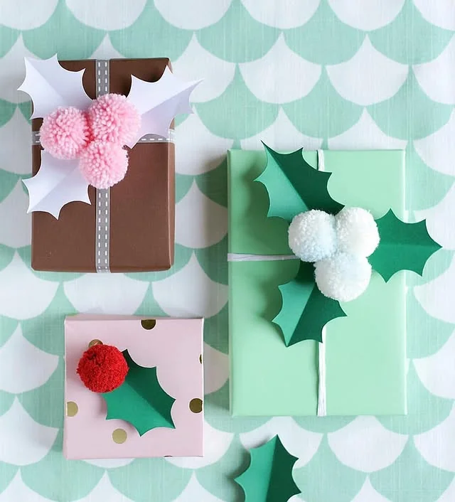 Pastel wrapped gifts topped with paper holly leaves and fluffy pom poms