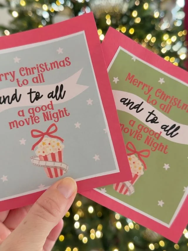 Printable movie night cards reading Merry Christmas held before a Christmas tree