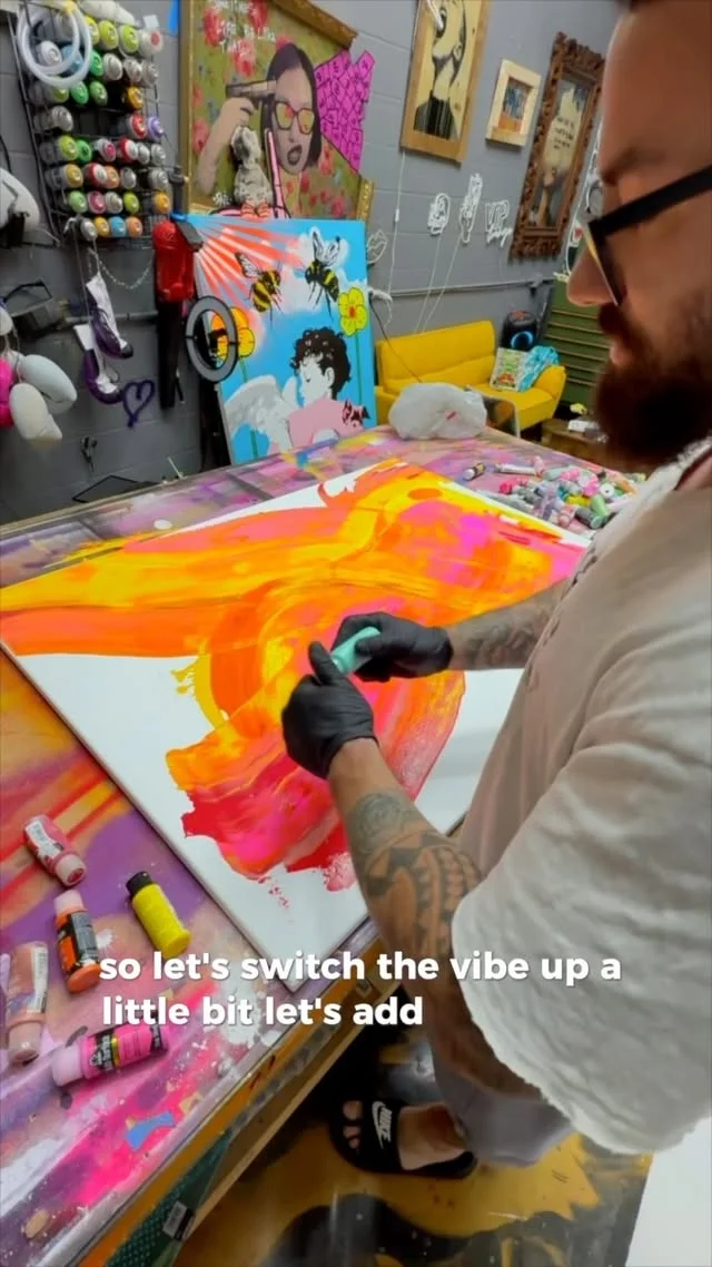 Artist using a foam tool to blend bold orange and pink swirls across a large white canvas