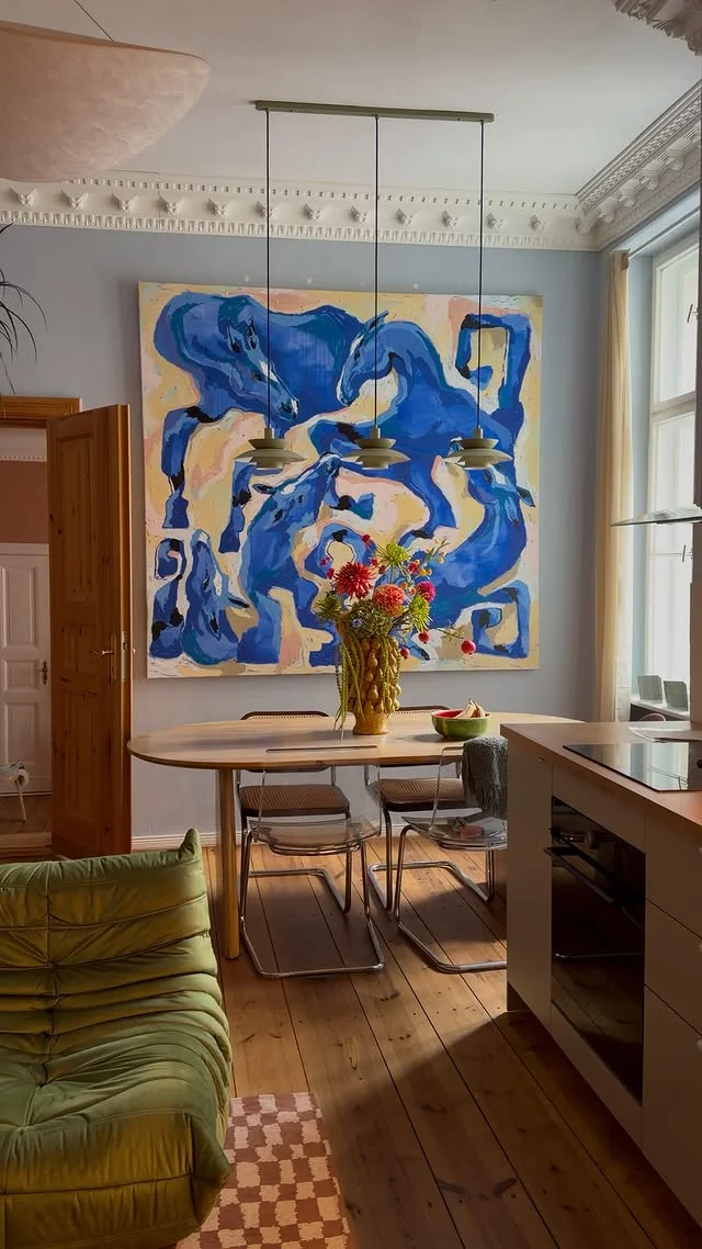 Large blue abstract painting with swirling shapes hanging above a dining table in a bright room