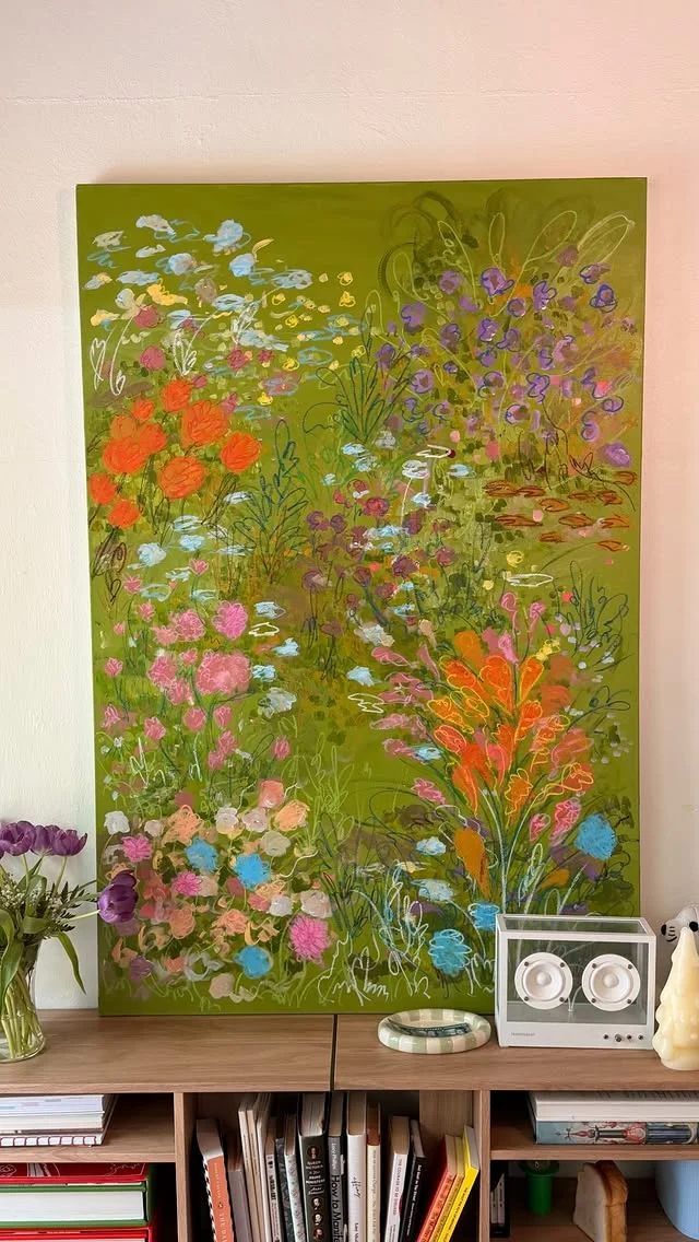 Large colorful abstract painting with green, orange and pink floral shapes above a wooden bookshelf