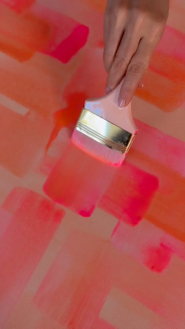 Hand painting wide peach and pink blocks across a canvas with a large flat brush