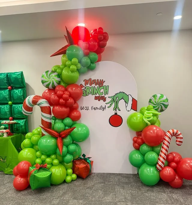 White arch backdrop with Merry Grinchmas lettering and balloon garland