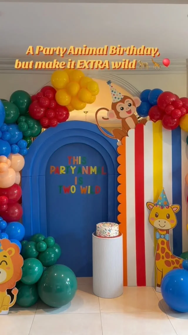 A bright blue arch with cartoon animals in party hats and a cake on a pedestal makes a loud first impression