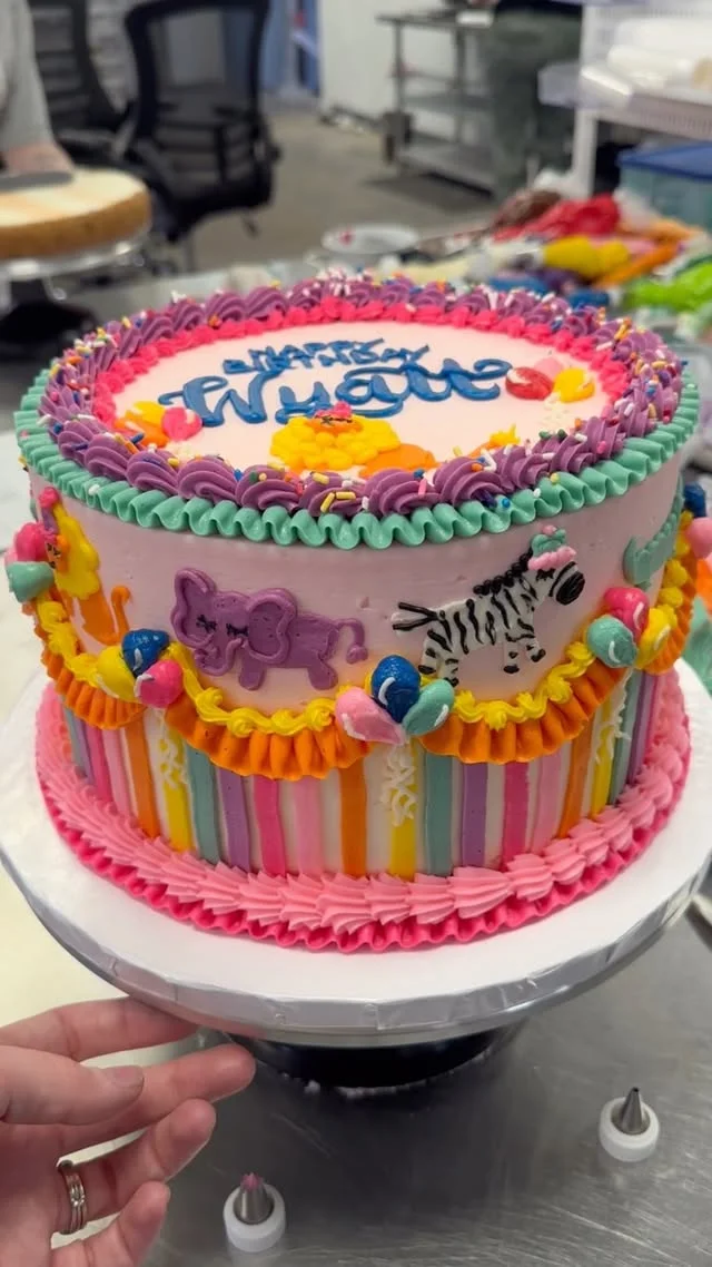 Pink circus cake with rainbow stripes and piped cartoon animals