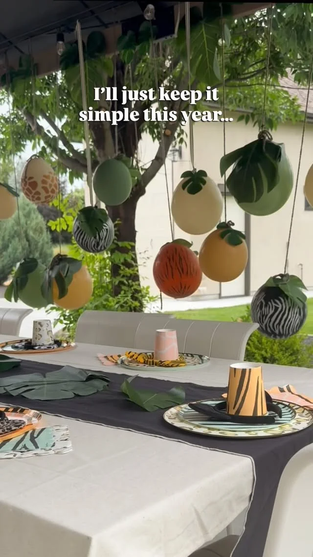 Animal print balloons hanging above a party table with jungle leaves