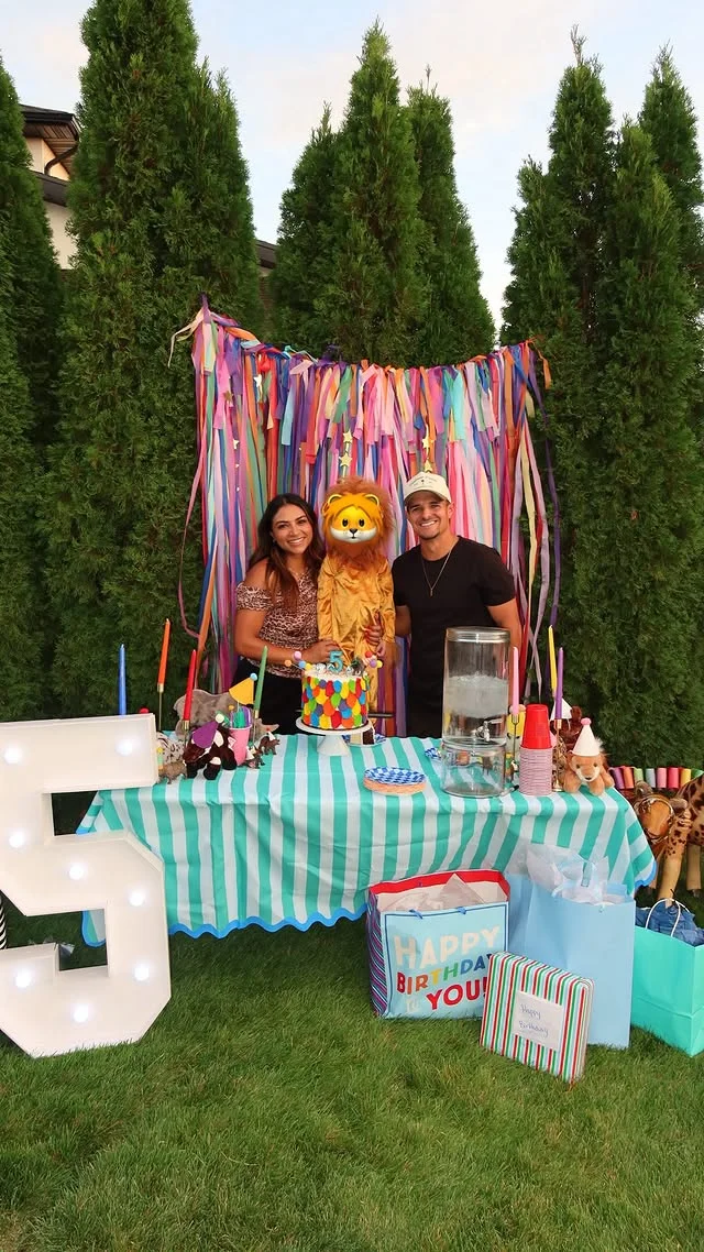 Backyard party table with striped cloth, animal masks and a rainbow cake