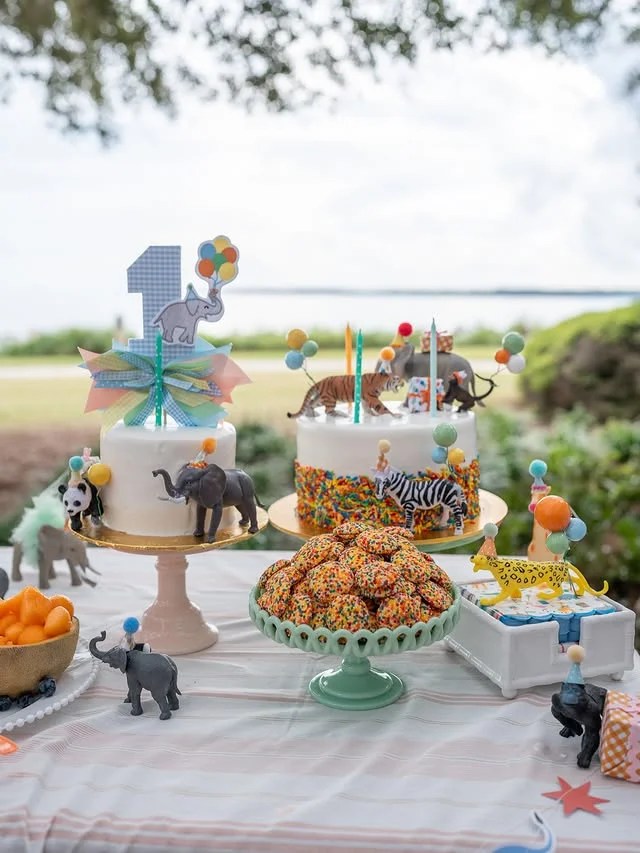 Outdoor dessert table with animal figurine cakes, cookies and a balloon number