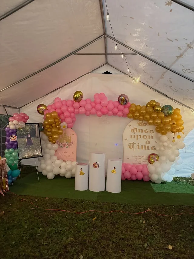 Outdoor tented party backdrop with a pink gold and white balloon arch and princess foil balloons
