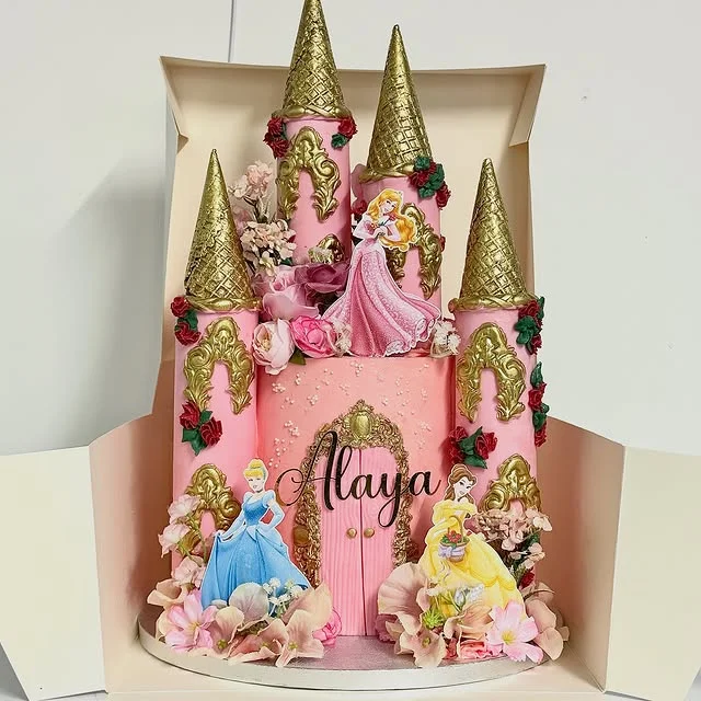 Pink castle cake with gold cone roofs inside an open box