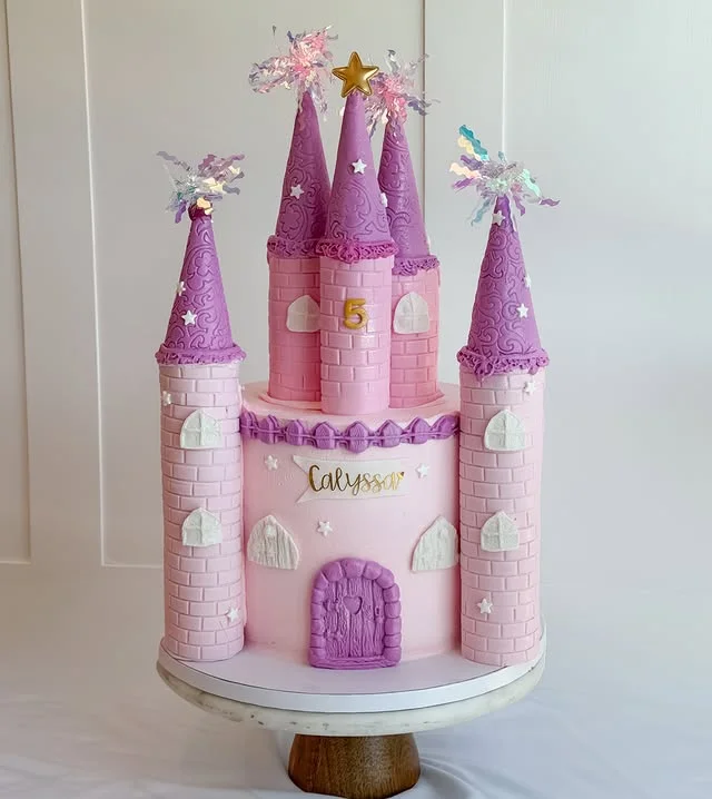 Pink and purple castle cake on a white cake stand