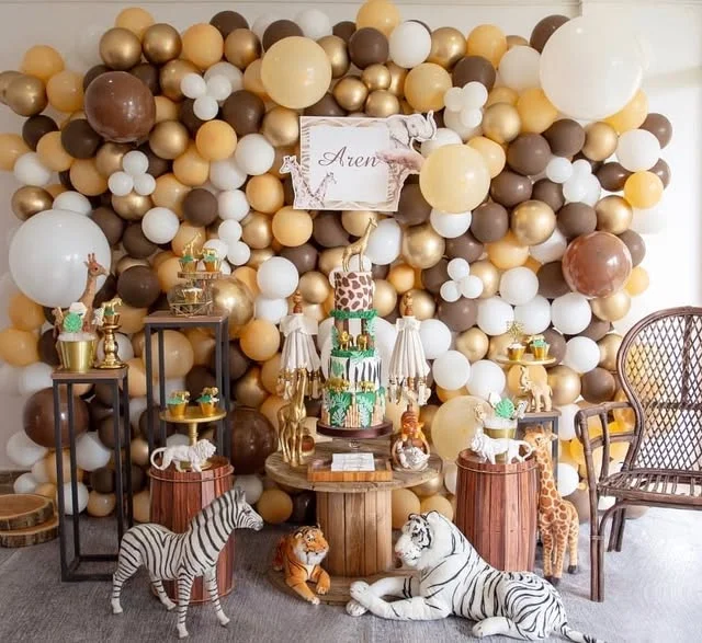 Brown, cream and gold balloon wall behind a cake table with standing animal figures