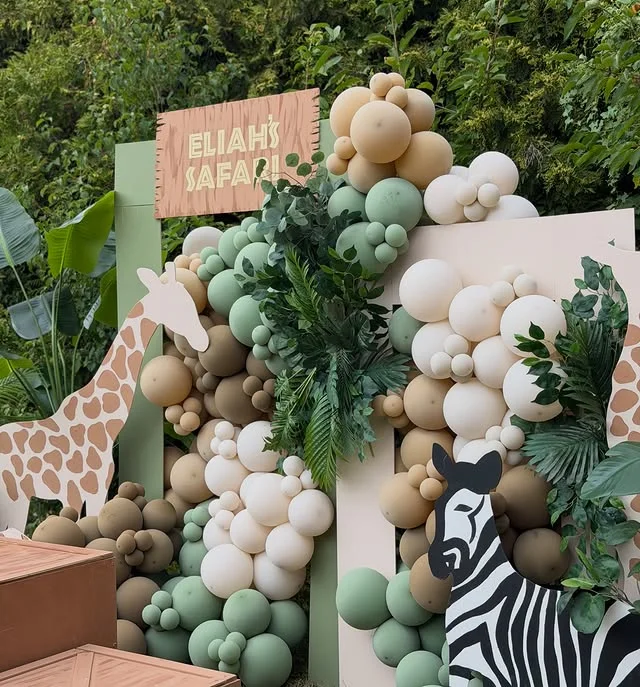 Wooden name sign on a sage and cream panel with a balloon garland and giraffe and zebra cutouts