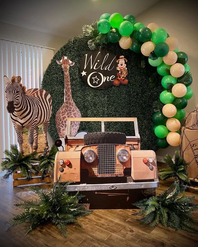 Toy jeep in front of a leafy Wild One backdrop with a green and cream balloon arch