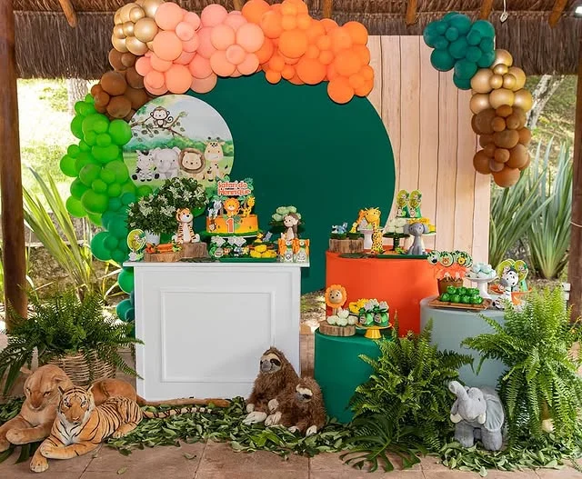 Green arch panel with a bright balloon top over a dessert table with plants and animal figures