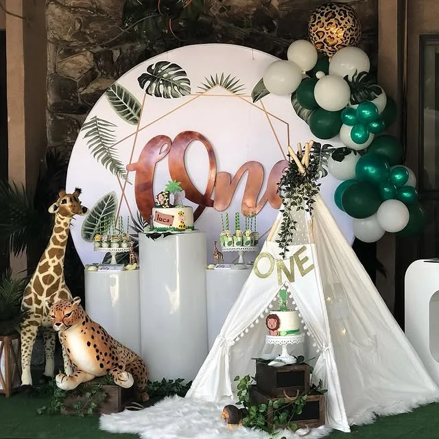White teepee beside a cake table with a round leaf backdrop and giraffe figure