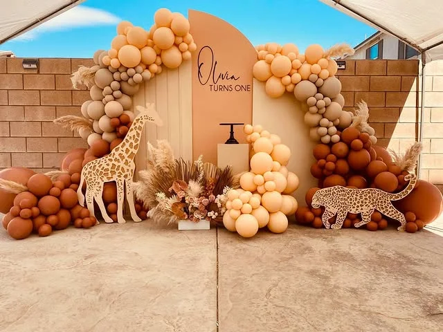 Cream and tan balloon arch around an outdoor panel with a giraffe figure
