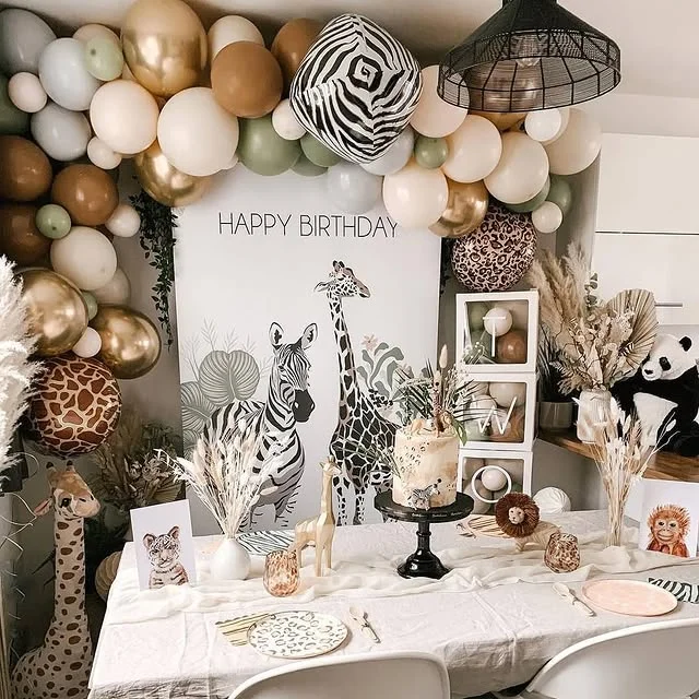 Neutral animal print backdrop with a balloon arch over a party table with a cake