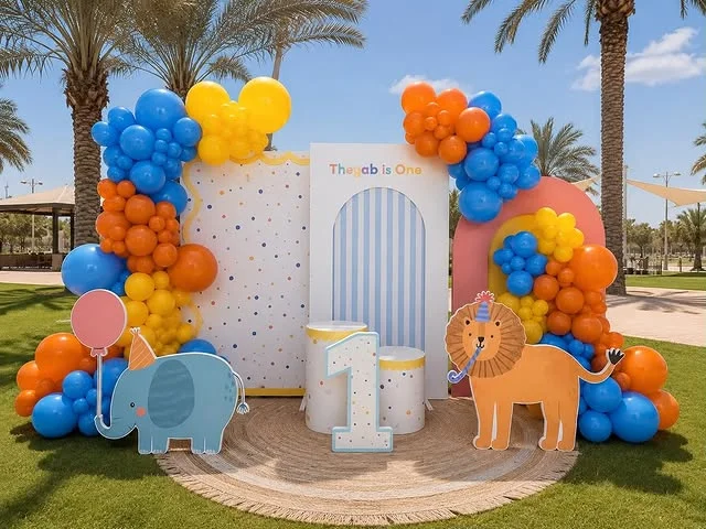 Outdoor Wild One party backdrop with lion and elephant cutouts and colorful balloons