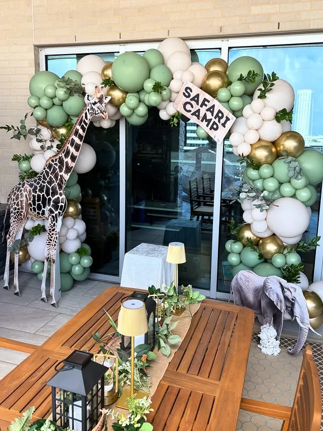 Safari Camp balloon arch with a tall giraffe cutout beside a wooden table